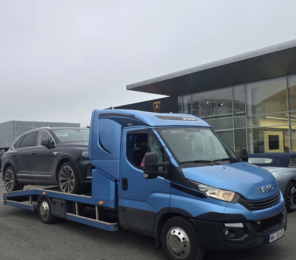 Tractări auto Vrancea - platforma albastră Iveco cu vehicul încărcat lângă showroom auto