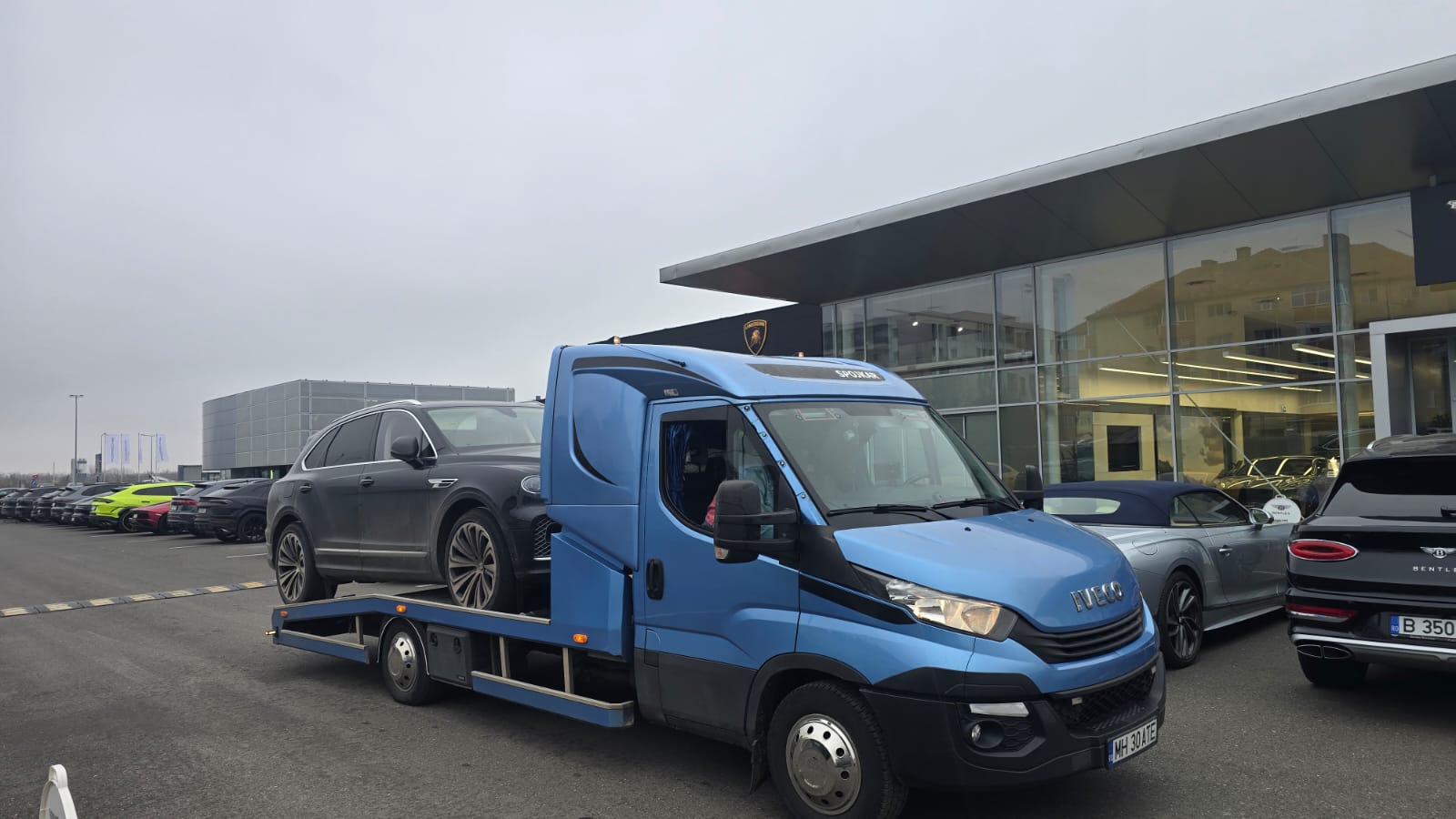 Tractări auto Vrancea - platforma albastră Iveco cu vehicul încărcat lângă showroom auto